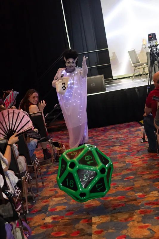 @thelolapalooza works the aisle with a mic and a money bag as a giant inflatable d20 flies past.