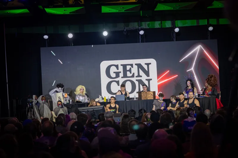 The full cast and crew at the long table on the Gen Con 2026 main stage, in front of a packed room.