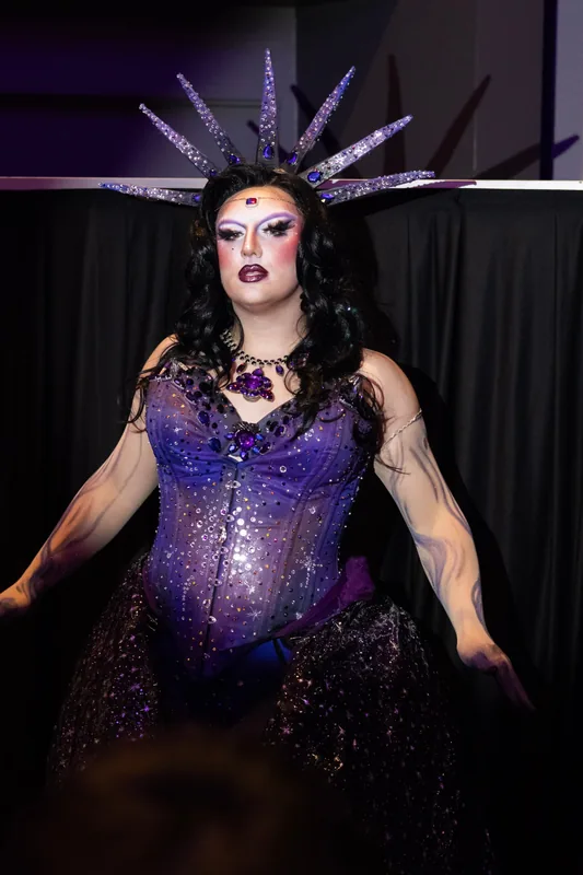@ilanaalamode in a purple jeweled corset and a tall spiked crown.